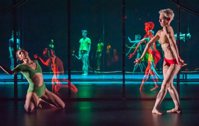 Two dancers in florescent leotards and trunks are reflected in the mirror set, multiplying their image countless times